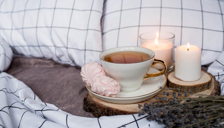 Wooden tray with tea, marshmallows, candles and lavender on the bed. White sheets with a striped...