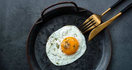 Homemade fried egg in a vintage pan and stylish cutlery on a dark background. view from above. Copy space for text.の写真素材
