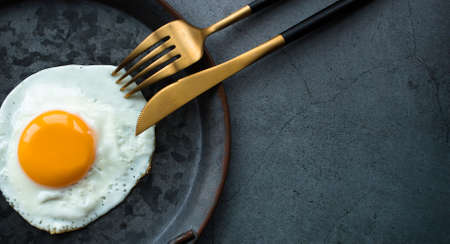 Homemade fried egg in a vintage pan and stylish cutlery on a dark background. view from above. Copy space for text.の写真素材