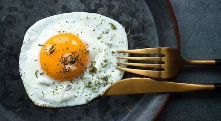 Homemade fried egg in a vintage pan and stylish cutlery on a dark background. view from above. Copy...