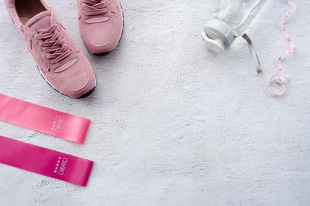 Banner. Healthy lifestyle and fitness in sports, morning jogging. Sneakers, fitness elastic bands, smart fitness tracker, tape measure and a water bottle on a gray background. Top view and flat lay.の写真素材