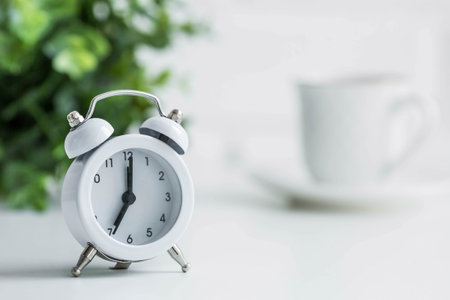 The concept of good morning time. White retro alarm clock, flowers and a cup of coffee on the...