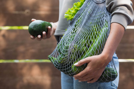 A woman's hand with an ecological shopping bag, buying vegetables, isolated on a white background. A...