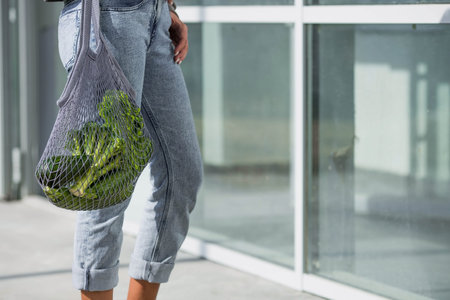 A modern stylish woman with a shopping bag, buying green vegetables against the background of the...
