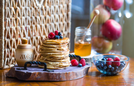 Delicious pancakes with honey, blueberries and raspberries. Next to it is a wooden barrel with an...