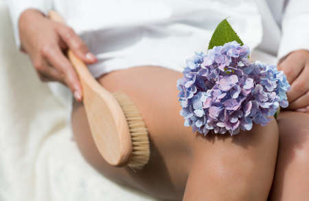 Cosmetology, grooming, peeling, spa cosmetic products, beauty and bikini concept. close-up Woman in white makes a foot massage with a wooden soft massage brush for body and feet.の写真素材