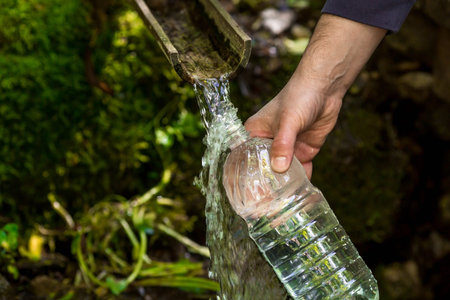 Male hands close-up, pouring clean drinking water from a holy spring into a plastic bottle.