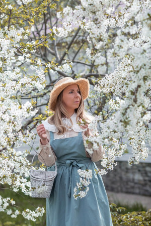 Vintage. A beautiful, young woman in retro clothes and a straw hat in a blooming cherry orchard. Boho style. Visual for content.の写真素材