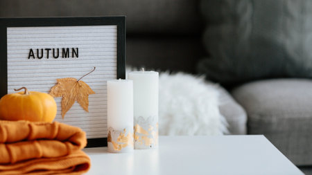 Autumn mood, cozy home interior with autumn decor, pumpkins, candles, maple leaves on a white tableの写真素材