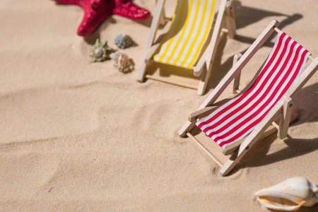 A toy beach chaise longue, seashells, a starfish on white sand with shadows. Sunlight. The concept of the sea, a beach holiday and a resort. summer minimalism.の写真素材