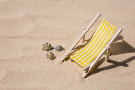 A toy beach chaise longue, seashells, a starfish on white sand with shadows. Sunlight. The concept of the sea, a beach holiday and a resort. summer minimalism.の写真素材