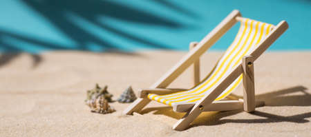 A toy beach chaise longue, seashells, a starfish on white sand with shadows. Sunlight. The concept of the sea, a beach holiday and a resort. summer minimalism.の写真素材