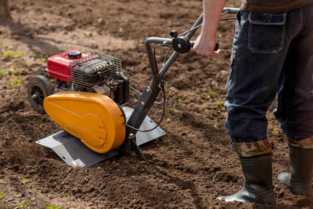 Banner. A male farmer plows the land with a cultivator. Agricultural machinery for tillage in the garden, combine harvester.の写真素材