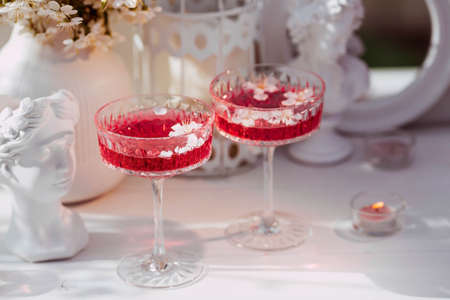 Two fashionable glasses for dessert and champagne with a pink drink and cherry blossoms inside on a light background with hard shadows and highlights. The concept of a party and a holiday.の写真素材