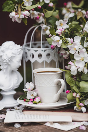 A beautiful postcard. A white coffee cup with a saucer, a statuette, candles, a book and a vase with...