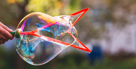 A man's hand makes big huge bright soap bubbles against the background of trees. Soap bubble show. Summer children's active recreation. Abstract blurred background.の写真素材