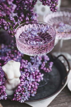 A candle and fancy glasses for dessert and champagne with a lilac drink and lilac flowers inside....