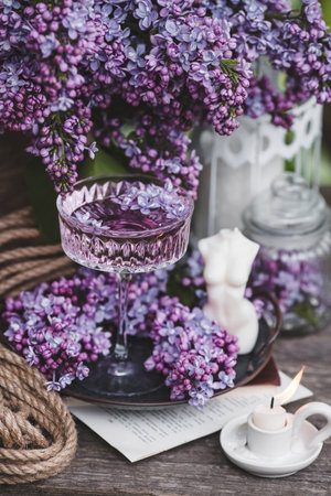 A candle and fancy glasses for dessert and champagne with a lilac drink and lilac flowers inside. The fashionable shade of 2022 is very relevant. The concept of a party and a holidayの写真素材