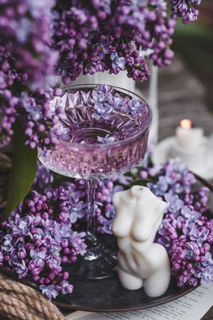 A candle and fancy glasses for dessert and champagne with a lilac drink and lilac flowers inside. The fashionable shade of 2022 is very relevant. The concept of a party and a holidayの写真素材