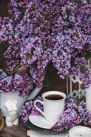 A bouquet of lilacs and a cup of coffee on a wooden tableの写真素材