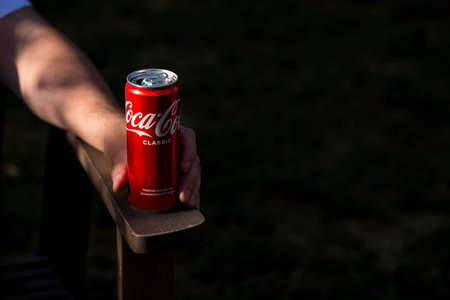 Moscow, May 2022: A crumpled Coca-Cola can on a wooden countertop in his hand. American soft drink. Prohibition for diabetics. Suspension of the company's activities in Russia.のeditorial素材