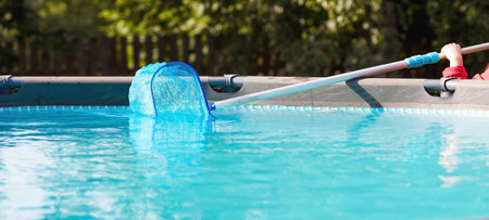 Cleaning a swimming pool with a metal frame with a net from leaves and dirt. Pool cleaner during...