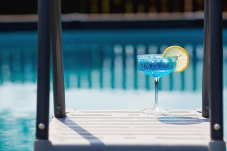 A glass of delicious blue cocktail Blue Lagoon and yellow lemons on the background of the pool....
