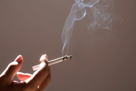 Close-up of a woman's hand holding a cigarette. Tobacco butt with clouds of smoke. Nicotine...