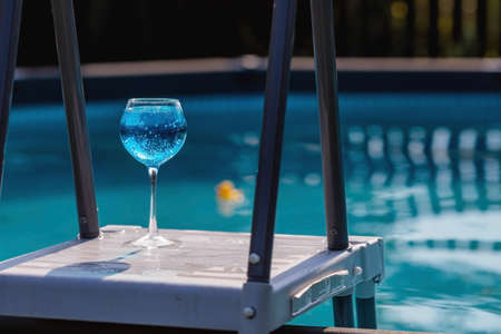 A glass of delicious blue cocktail and yellow lemons on the background of the pool. Alcoholic cocktail juicy fruit blue with curacao liqueur, ice cubes and a slice ofの写真素材