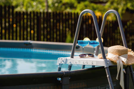 A glass of delicious blue cocktail  and yellow lemons on the background of the pool. Alcoholic cocktail juicy fruit blue with curacao liqueur, ice cubes and a slice ofの写真素材