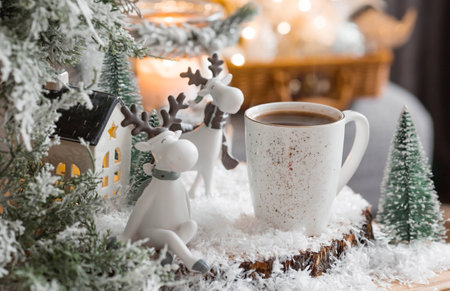A Christmas card with cute reindeer and a mug of hot coffee on the background of a beautiful bokeh. New Year's still life. The concept of a home holiday, warmth and comfort.の写真素材