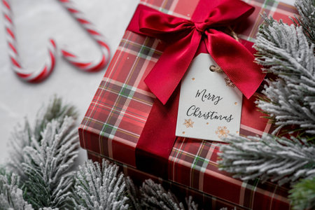 A red gift box, spruce branches, candy cane and a label with the inscription merry Christmas on a gray marble background. Christmas holidays 2023. Buying and preparing gifts for faの写真素材