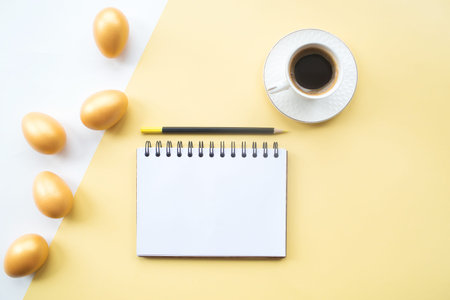 Golden Easter eggs, a coffee mug and a notebook with a place for text on a yellow background....