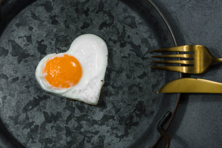 Homemade fried egg in a vintage pan, mug of coffee, hearts and stylish cutlery on a dark background....