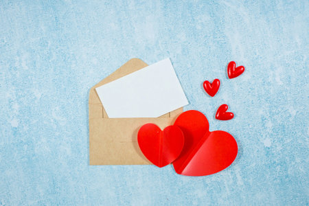 Red hearts, an envelope, and a white sheet of paper for text on a blue background with copy space....