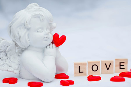 The word "Love" and a cute angel on a white, marble background. Love on wooden cubes. Theme of love. Valentine's day. Wooden blocks with the word love. positive emotion.の写真素材