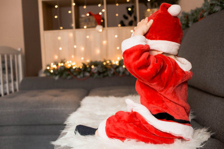 A beautiful little boy in a Santa Claus costume with light bulbs in his hands on the background of Christmas lights. The concept of Christmas celebration. new year holiday.の写真素材