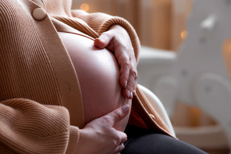 A young pregnant woman holding her tummy against the background of a Christmas tree. close-up. A woman is preparing to become a mother. A gift for the new year. Pregnancy and childbirth.の写真素材