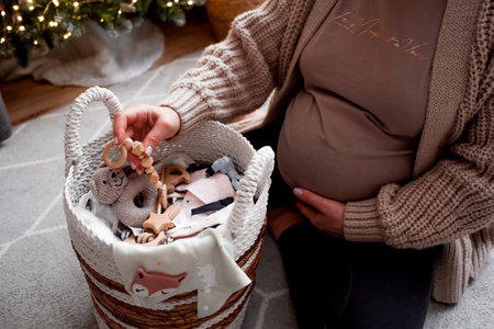 A young pregnant woman holding her tummy against the background of a Christmas tree. close-up. A woman is preparing to become a mother. A gift for the new year. Pregnancy and childbirth.の写真素材
