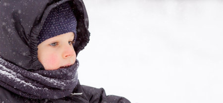 Portrait of a beautiful little Russian boy in winter in the park. Snow is falling. Cold. Red cheeks. The concept of a happy childhood and remedies for the skin from frost.の写真素材