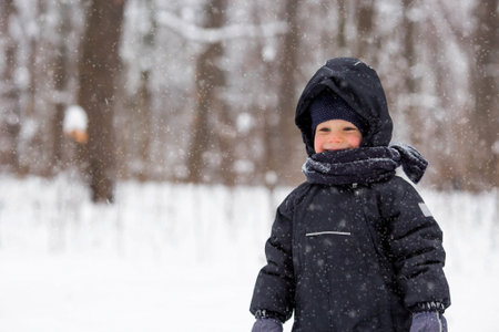 Portrait of a beautiful little Russian boy in winter in the park. Snow is falling. Cold. Red cheeks....