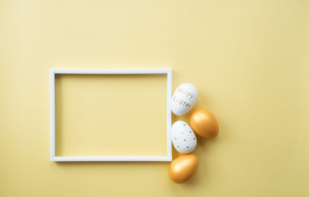 Golden easter eggs with white frame for text on a yellow background. Trendy flat lay easter. Minimal...