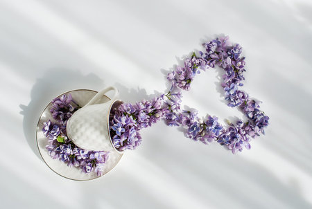 Cup and lilac flowers in the form of a heart on a white table. Love concept for background or copy...