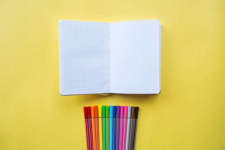 Colorful background with multi-colored pens and a notebook for text. School supplies lie on a bright...