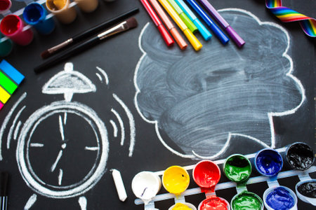 School supplies, paints, multi-colored pens, a drawn alarm clock and a cloud with copy space for text. Top view on a flat lay. The concept of a new school year at school.の写真素材