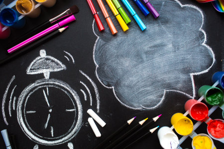 School supplies, paints, multi-colored pens, a drawn alarm clock and a cloud with copy space for text. Top view on a flat lay. The concept of a new school year at school.の写真素材