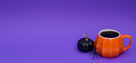 Orange coffee cup in the shape of a pumpkin on a fashionable purple background. The concept of a festive morning for Halloween.の写真素材