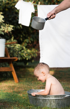 A little boy bathes, washes in an iron basin. A happy child splashes in the water. vintage. The concept of child hygiene. Soap bubbles, a bubble bath.の写真素材