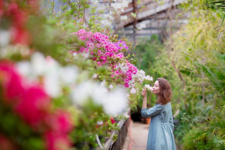 Beautiful young girl posing in a blooming garden. A pretty lady with brown wavy hair, dressed in a dress. Flower pots around the greenhouse. Tenderness female model photo session in a flower greenhouseの写真素材