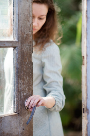 Beautiful young girl posing in a blooming garden. A pretty lady with brown wavy hair, dressed in a dress. Flower pots around the greenhouse. Tenderness female model photo session in a flower greenhouseの写真素材